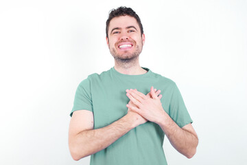 Honest young handsome caucasian man wearing green t-shirt against white background keeps hands on...