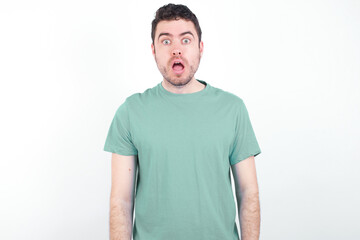 Obraz premium Emotional attractive young handsome caucasian man wearing green t-shirt against with opened mouth expresses great surprise and fright, stares at camera. Unexpected shocking news and human reaction.