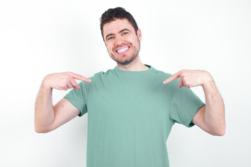 Pick me! Confident, self-assured and charismatic young handsome caucasian man wearing green t-shirt against white background promoting oneself as wanting role smiling broadly and pointing at body.