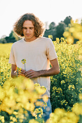 young man with curly hair with a yellow flower in a rapeseed flower camp
