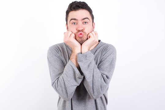 young handsome caucasian bearded man wearing pyjama over white wall with surprised expression keeps hands under chin keeps lips folded makes funny grimace