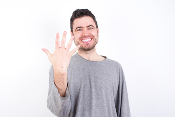 Fototapeta premium young handsome caucasian bearded man wearing pyjama over white wall smiling and looking friendly, showing number five or fifth with hand forward, counting down
