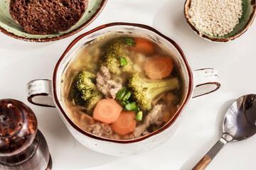 Top view of homemade soup with meat and vegetables in white soup bowl, bread and a spoon on white background. Healthy lunch, dinner. Stock photo, copy space