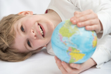The child dreamily examines the globe. Travel yearning concept. Closed borders and quarantine. A European-looking child dreams of travel