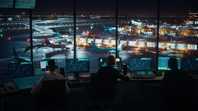 Diverse Air Traffic Control Team Working in a Modern Airport Tower at Night. Office Room is Full of Desktop Computer Displays with Navigation Screens, Airplane Flight Radar Data for Controllers.