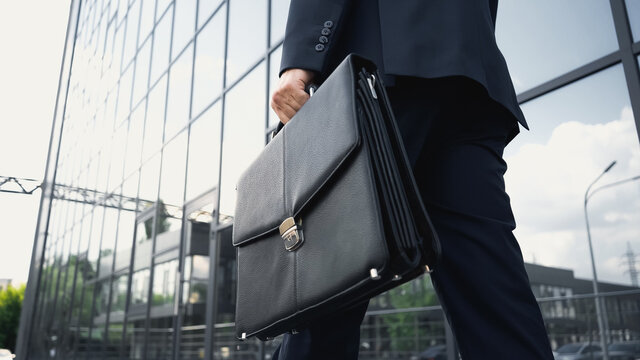 cropped view of businessman walking with leather briefcase.