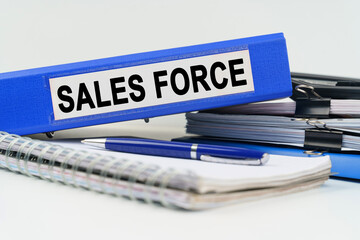 On the table are a notebook, a pen, documents and a folder with the inscription - SALES FORCE