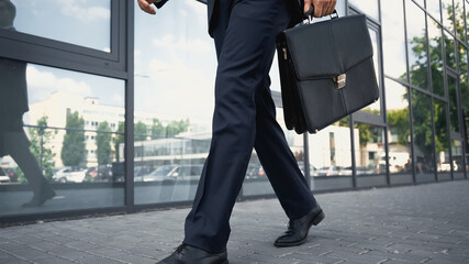 partial view of businessman in formal wear walking with briefcase outside.
