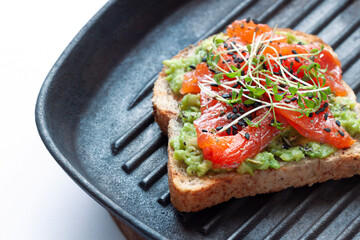 A Toast with salted salmon fish, avocado and young sprouting greens on the grill pan macro