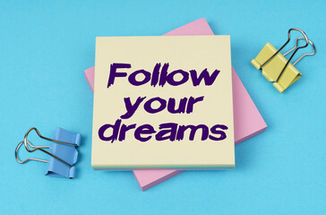 On the table are paper clips, note paper with text - Follow your dreams