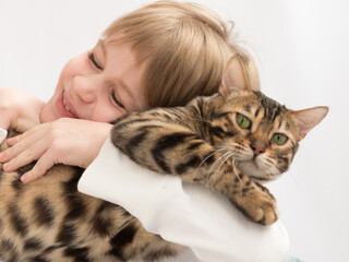 The child hugs the cat tightly. The cat is unhappy. Love to the animals. Enjoyment of communication. Close-up portrait