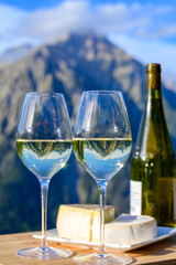 Tasty cheese and wine from Savoy region in France,  tomme and reblochon de savoie cheeses and glass of white wine served outdoor with Alpine mountains peaks on background