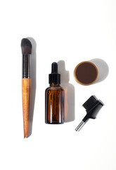 Obraz premium A set for face skin care: serum in a jar with a pipette, cream, brush and eyebrow brush isolated on a white background. Top view