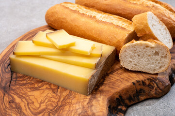 French food -  piece of cheese comte made from cow milk in region Franche-Comte in France and fresh baked baguette bread.