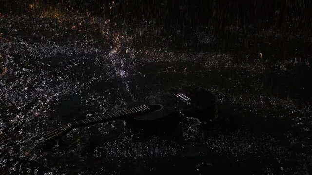 Top view wooden acoustic guitar hits the surface of water, creating a lot of splashes. Musical instrument in the rain. Guitar among the raindrops on a black studio background. Close up. Slow motion.