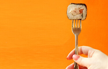 The hand holds a fresh sushi roll with a fork, insulated against an orange background. How to eat...