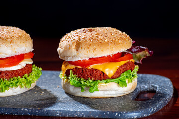 Tasty vegetarian food, homemade cheeseburgers made from plant based soya meat with cheese, onion, green lettuce and tomatoes
