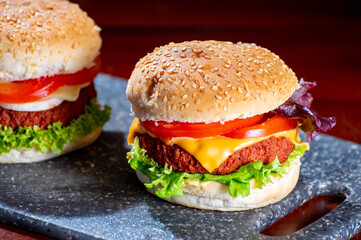 Tasty vegetarian food, homemade cheeseburgers made from plant based soya meat with cheese, onion, green lettuce and tomatoes