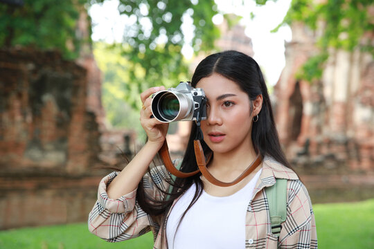 Potrait young woman toruist holding a camera , shooting a photo during outdoor travel at Ayutthaya historical part one place of World heritage
