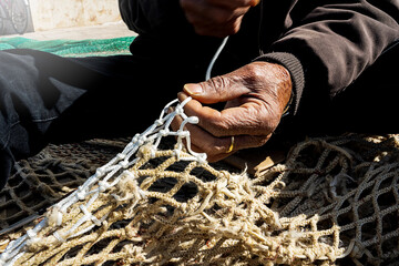 old fisherman hand sews a fishing net