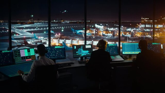 Diverse Air Traffic Control Team Working in a Modern Airport Tower at Night. Office Room is Full of Desktop Computer Displays with Navigation Screens, Airplane Flight Radar Data for Controllers.