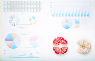 Top view, desktop - business documents, financial charts and two donuts. Breakfast in the office.