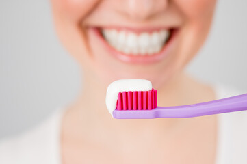 A woman with a snow-white smile holds a toothbrush with paste on a white background