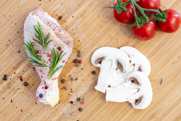 Fresh raw chicken drumstick leg with rosemary, spices, tomatoes, mushrooms  and olive oil on kitchen cutting board 