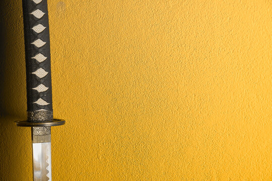 A closeup of Japanese sword katana isolated on yellow background wall. Sword used for martial arts such as kenjutsu, ninjutsu and battojutsu.