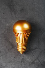 Gold light bulb on a black textured background.