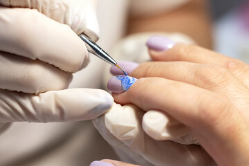 Obraz na płótnie Canvas Nail design. The process of coating the nails with gel polish and drawing the design with a brush by a specialist in a beauty salon. Close-up. Space for text