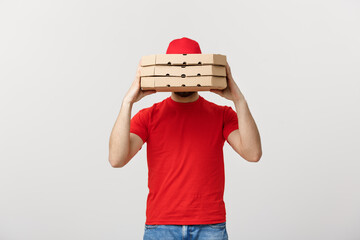 A Deliveryman hidden behind a large stack of pizza boxes he is carrying. Isolated over grey background.