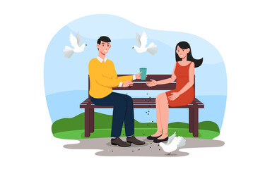 Young couple is sitting on a bench in park and feeding pigeons