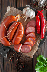 Homemade smoked sausage with garlic and chili on a round dark wooden board, top view
