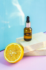 A cosmetic jar with an eyedropper stands on two granite slabs, like on catwalks, next to half a yellow lemon and the glare of the sun on the background. Cosmetics for summer