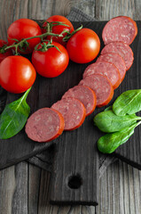 Smoked spiced sausage with tomatoes and basil on a wooden chopping board