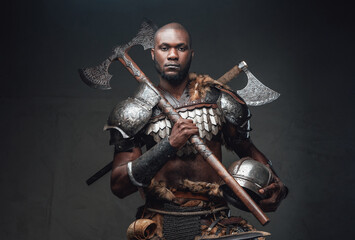 Serious fighter with black skin holding a helmet and an axe