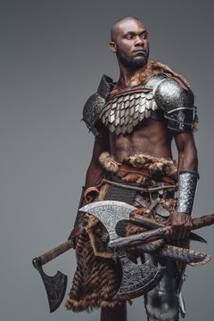 Portrait of a black skinned wild man with two huge axes in gray background