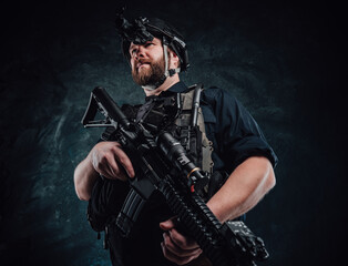 Fototapeta na wymiar Soldier with helmet and vest stays holding a rifle in dark background