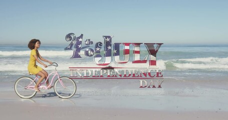 American flag waving over independence day text against woman riding bicycle on the beach