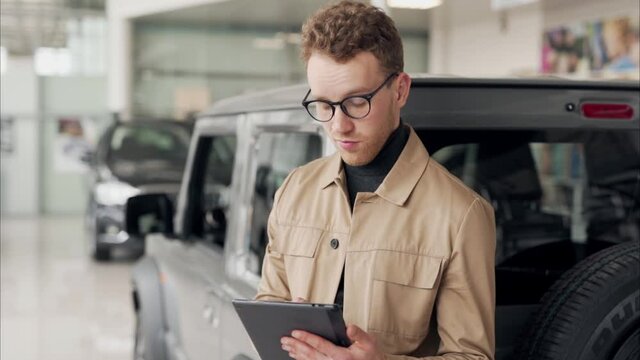 Stylish business man in glasses with a tablet in his hands on the background of cars in the showroom