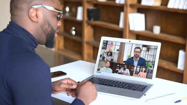 Male businessman with glasses and beard leads distant communication with multicultural colleagues using laptop app, discussing world social project, writing down plans and ideas, sitting at home