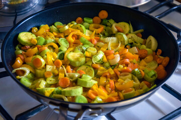 Vegetable saute in frying pan on gas stove. Process of cooking stewed vegetables at home. Ingredients leek, carrot, zucchini, bell pepper. Close-up. Selective focus.