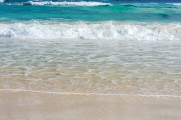 A foamy wave runs over the sandy beach. Seascape turquoise ocean and sandy coast against the blue sky. Rest by the sea. Exotic island.