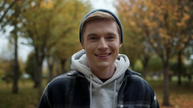 Cheerful handsome man posing for camera in autumn park. Guy looking at camera.