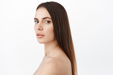 Fototapeta premium Beautiful woman with healthy long brunette hair, clean smooth skin, hydrated facial without wrinkles, anti-aging effect of cosmetics, turn head and look fashion, white background