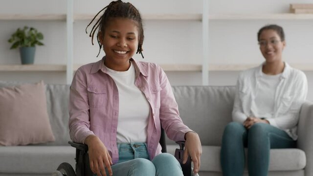 Happy Handicapped Black Girl In Wheelchair And Mother Sitting Indoor