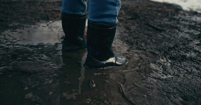 A baby girl in rubber boots jumps in a puddle. Spring weather, melting snow. Funny games on the street, warm spring weather. 4K