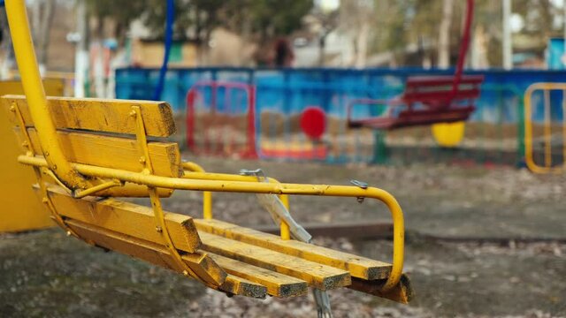 Lonely yellow empty deserted swing in an old abandoned amusement park. Swinging seat moving back and forth. Carousel swinslowly moves. Loneliness concept or child abduction. Dangerous area.Ghost town.
