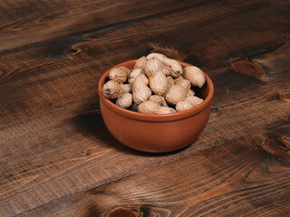 Unpeeled freshly roasted peanuts in a brown bowl on a wooden background